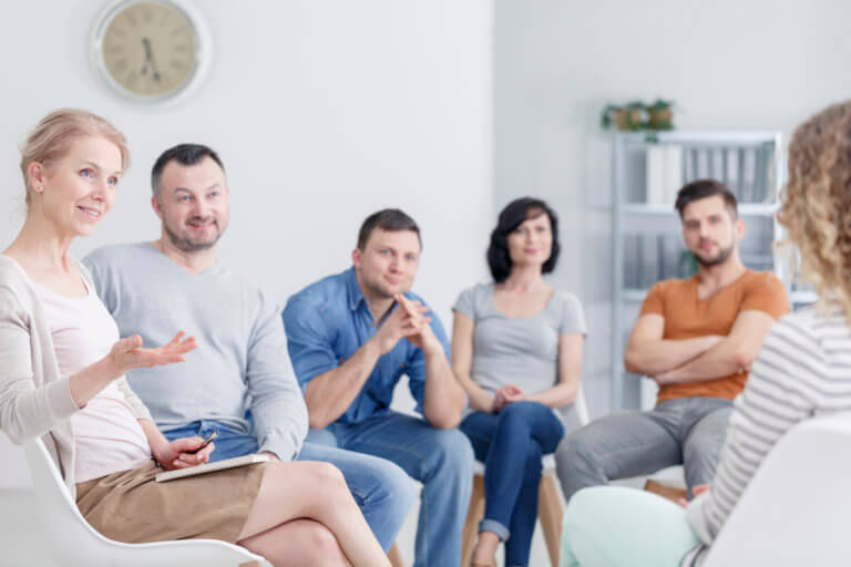 Therapist congratulating young woman on her progress in therapy and happy family in the background