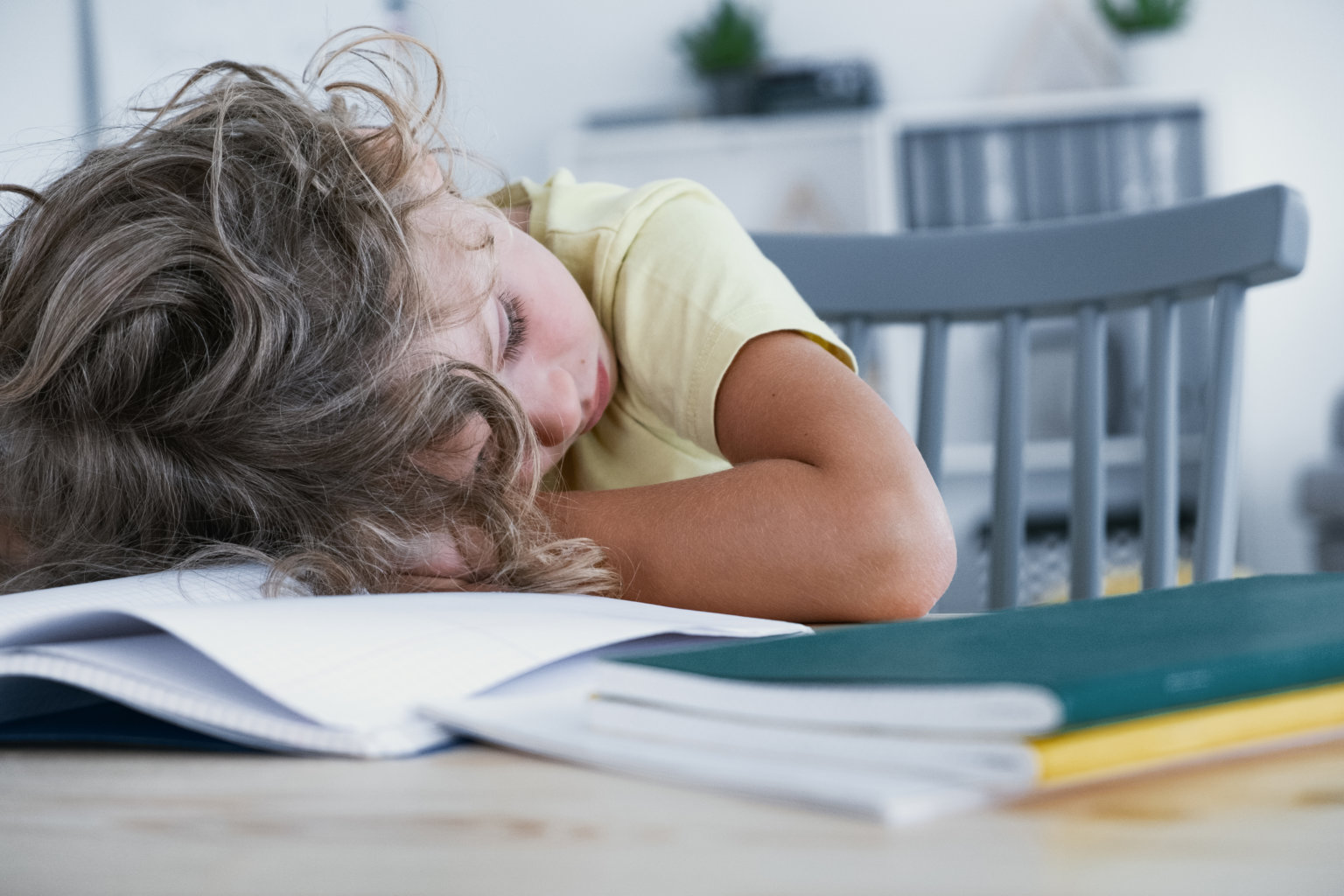 Close-up of a tired kid sleeping with his head rested on a table with a book.